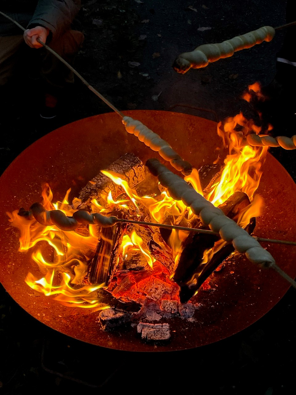  Über einer brennenden Feuerschale wird Stockbrot geröstet. 