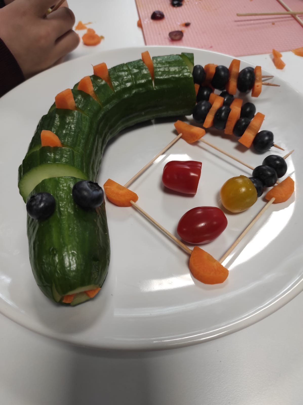  Eine Gurke, die mit anderen Obst- und Gemüsesorten zu einer Schlange drapiert wurde 
