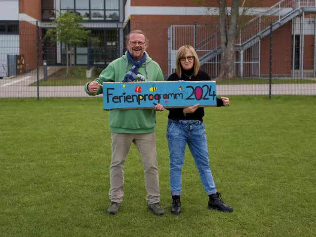 Jürgen und Fugmann und Lidija Zollner mit einem Schild mit der Aufschrift Ferienprogramm